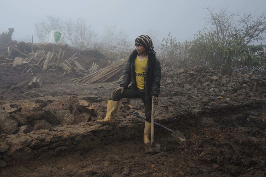 A Nepalese person stands next to the remains of a flattened house