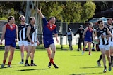 A Lilydale Demons player calls out to a teammate while on a football field surrounded by players from the opposing side.