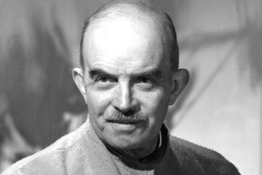 A black and white photo shows an older man looking earnestly above the camera.