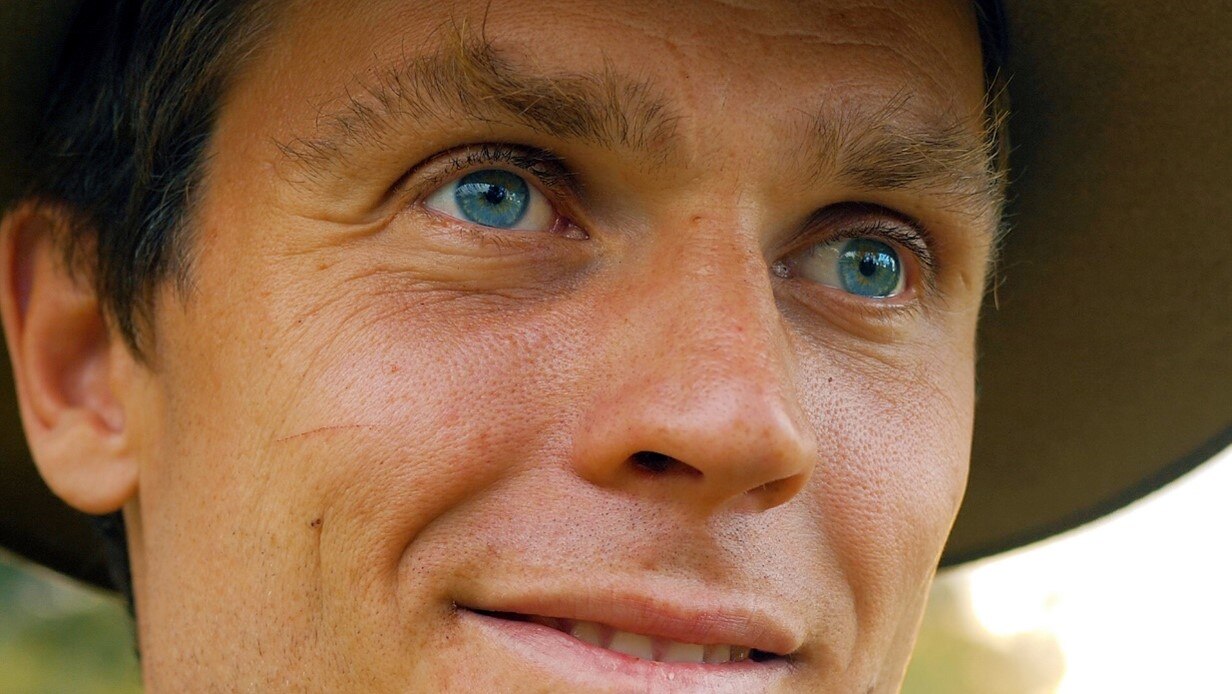 Very close shot of man's face with blue eyes, wearing a hat