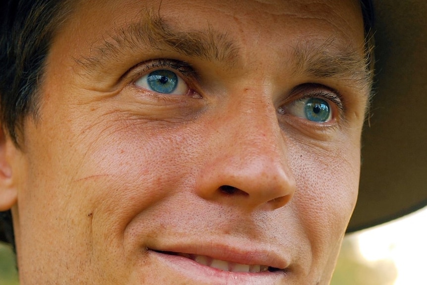 Very close shot of man's face with blue eyes, wearing a hat
