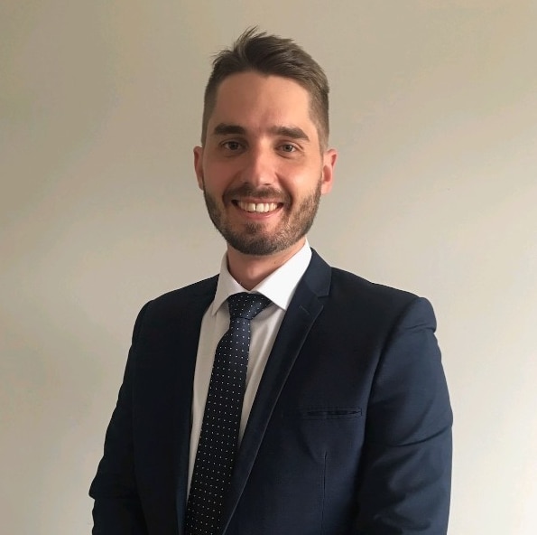 Una foto de retrato de un joven sonriente con traje y corbata 