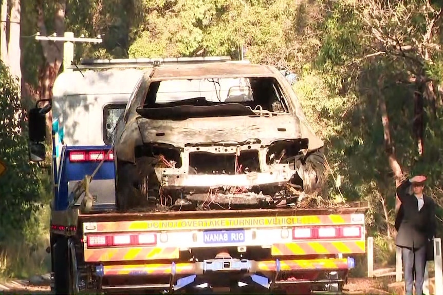 The shell of a burned-out car on the back of a tow truck.