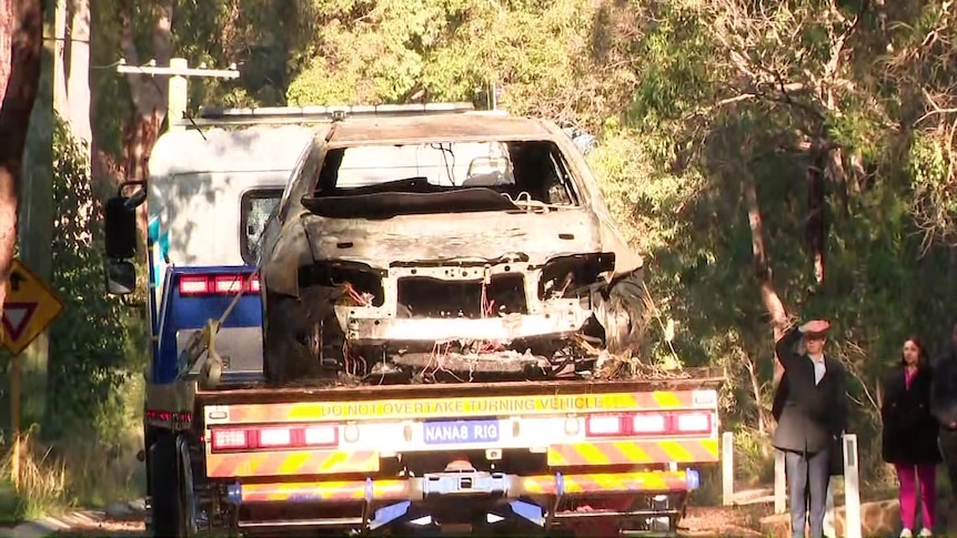 The shell of a burned-out car on the back of a tow truck.