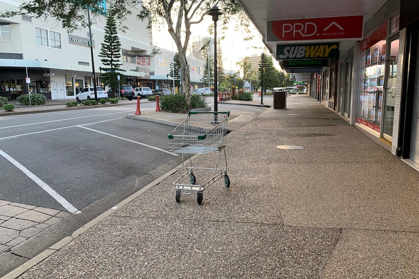 An empty city street with a lone shopping trolley on the footpath.