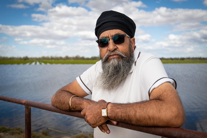 A man stands with his arms over a railing, with the river behind him