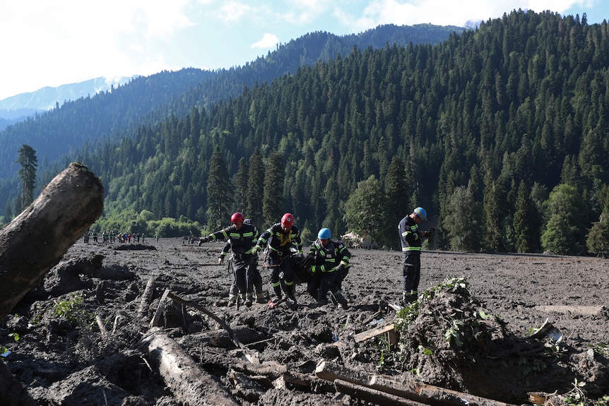 four emergency workers wearing helmets and high vis helping people surrounded with mud in a valley