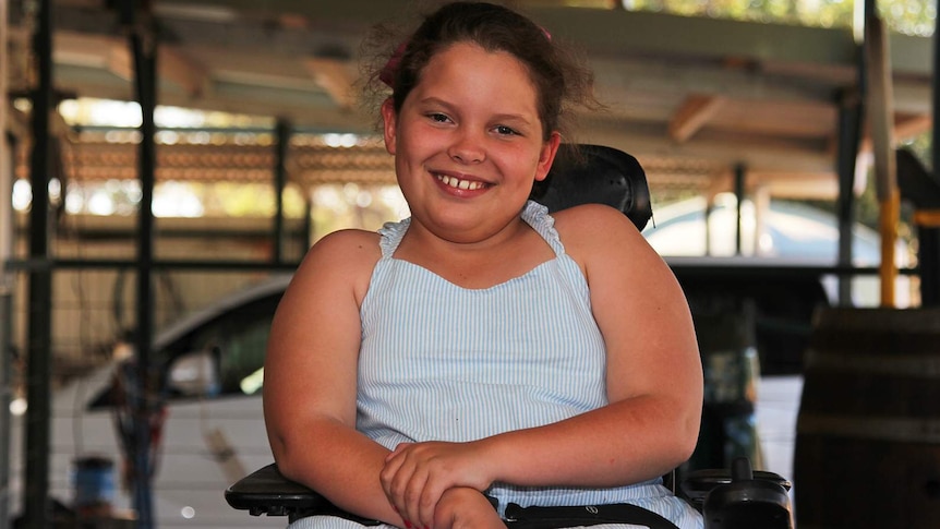 A photo of Katherine nine-year-old Felicity Brown in a wheelchair on the front deck of her house.