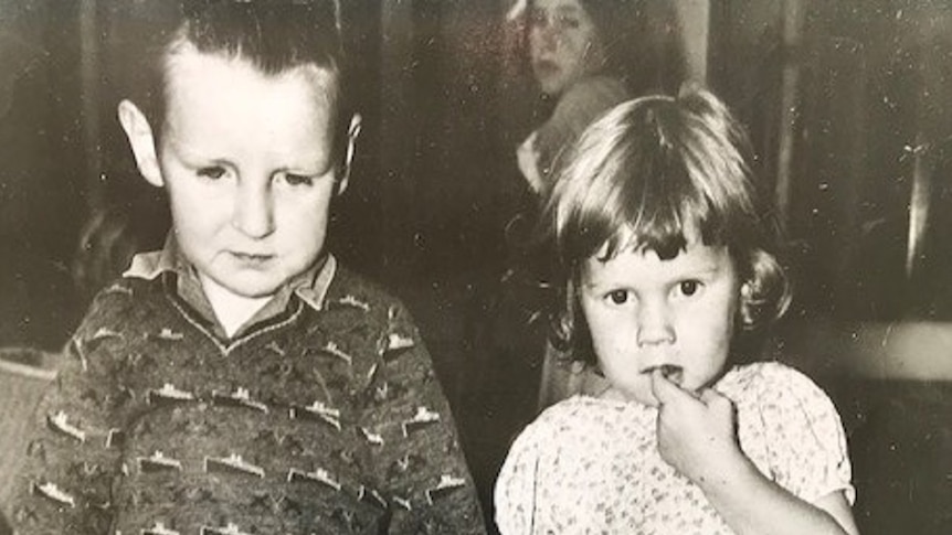 A young boy and a young girl stand side-by-side holding hands in a picture taken around 1951