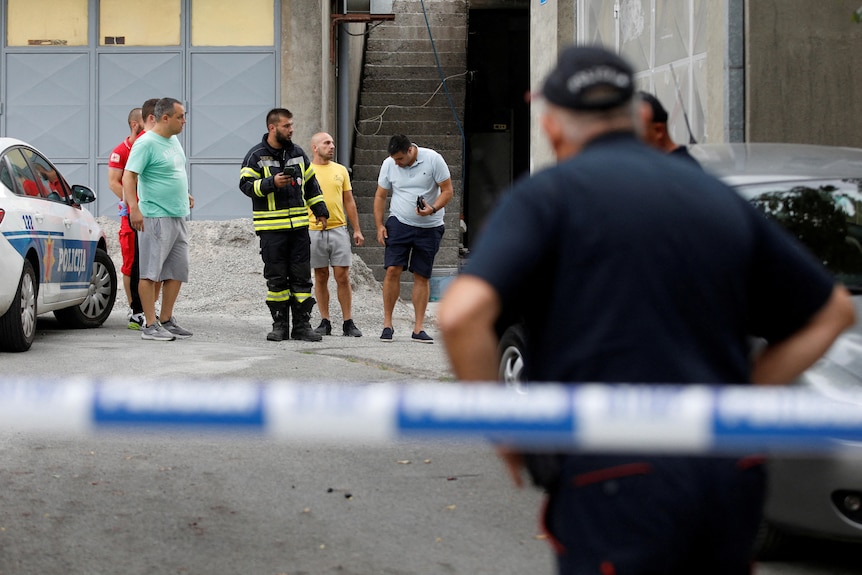 emergency service personnel and people stand behind police tape