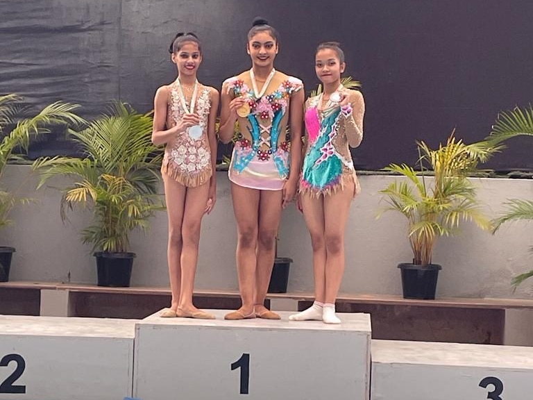 Three young women gymnasts stand on a medal podium holding medals.