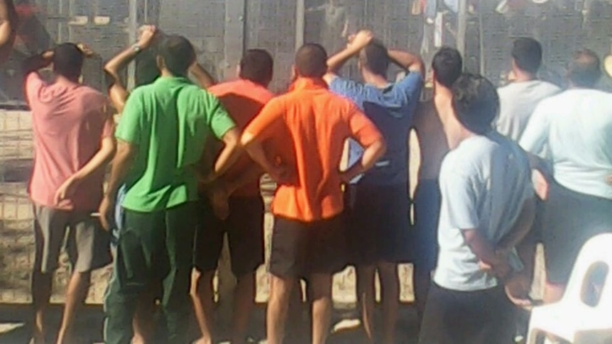 Asylum seekers stand against a fence at Manus Island detention centre