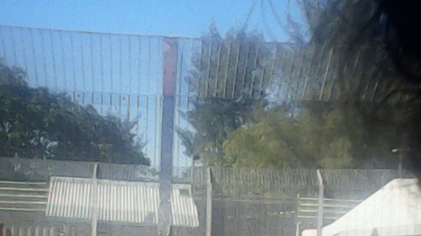 Asylum seekers stand against a fence at Manus Island detention centre