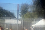 Asylum seekers stand against a fence at Manus Island detention centre