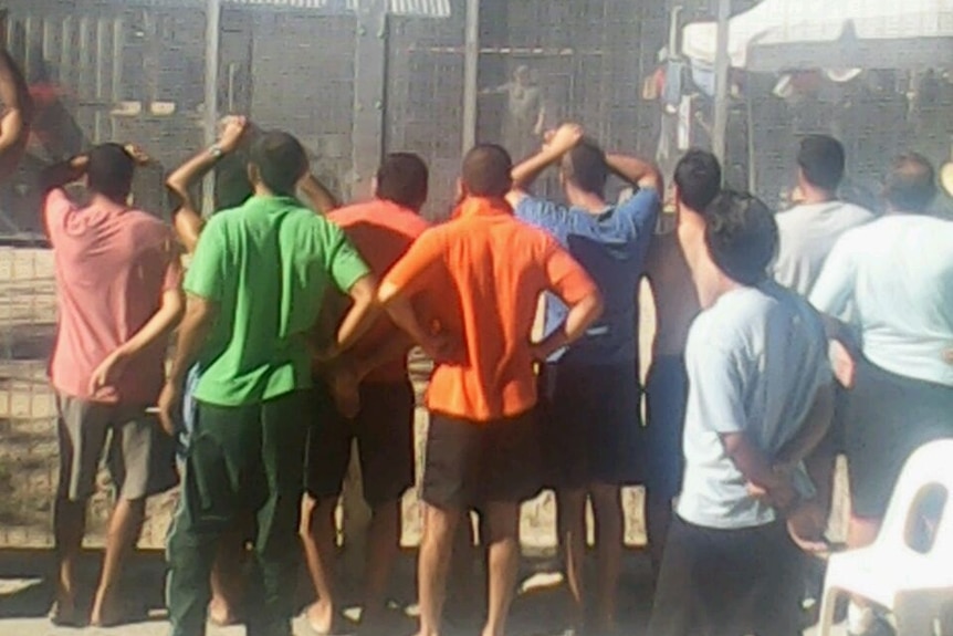 Asylum seekers stand against a fence at Manus Island detention centre