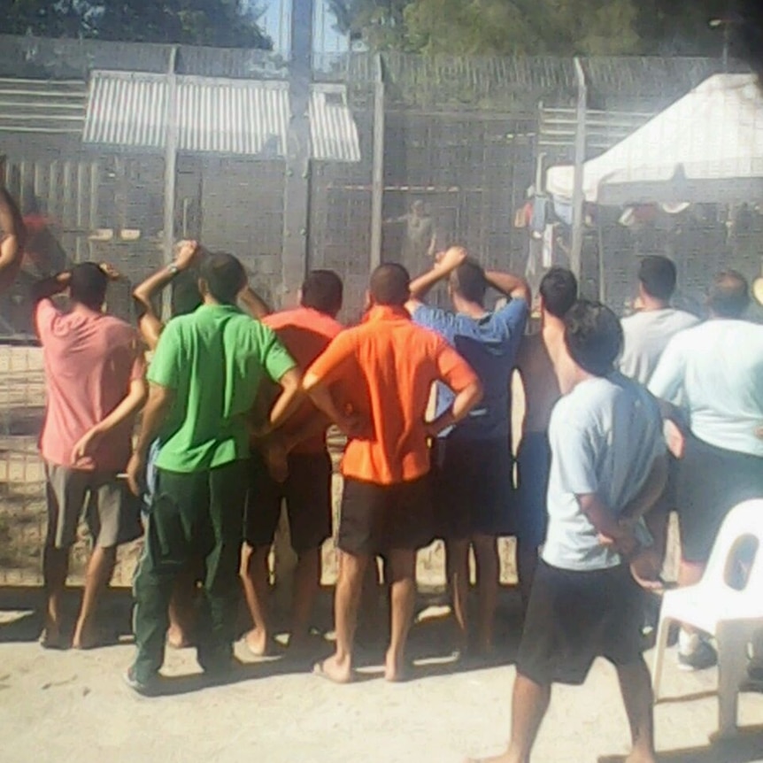 Asylum seekers stand against a fence at Manus Island detention centre