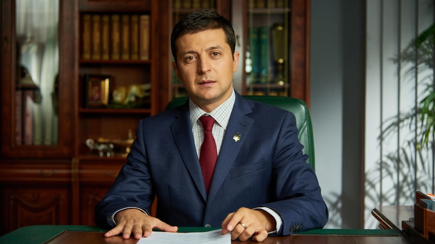 A young Volodymyr Zelenskyy sitting at a desk looking presidential in a TV still