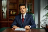 A young Volodymyr Zelenskyy sitting at a desk looking presidential in a TV still