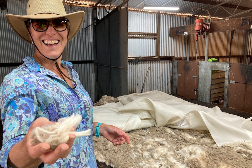 Woman holds handful of wool in working shearing shed on farm