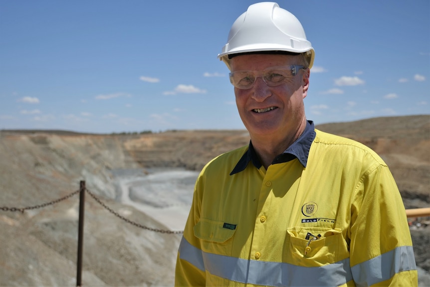 Man wearing hard hat and yellow fluoro shirt standing in from of mine pit