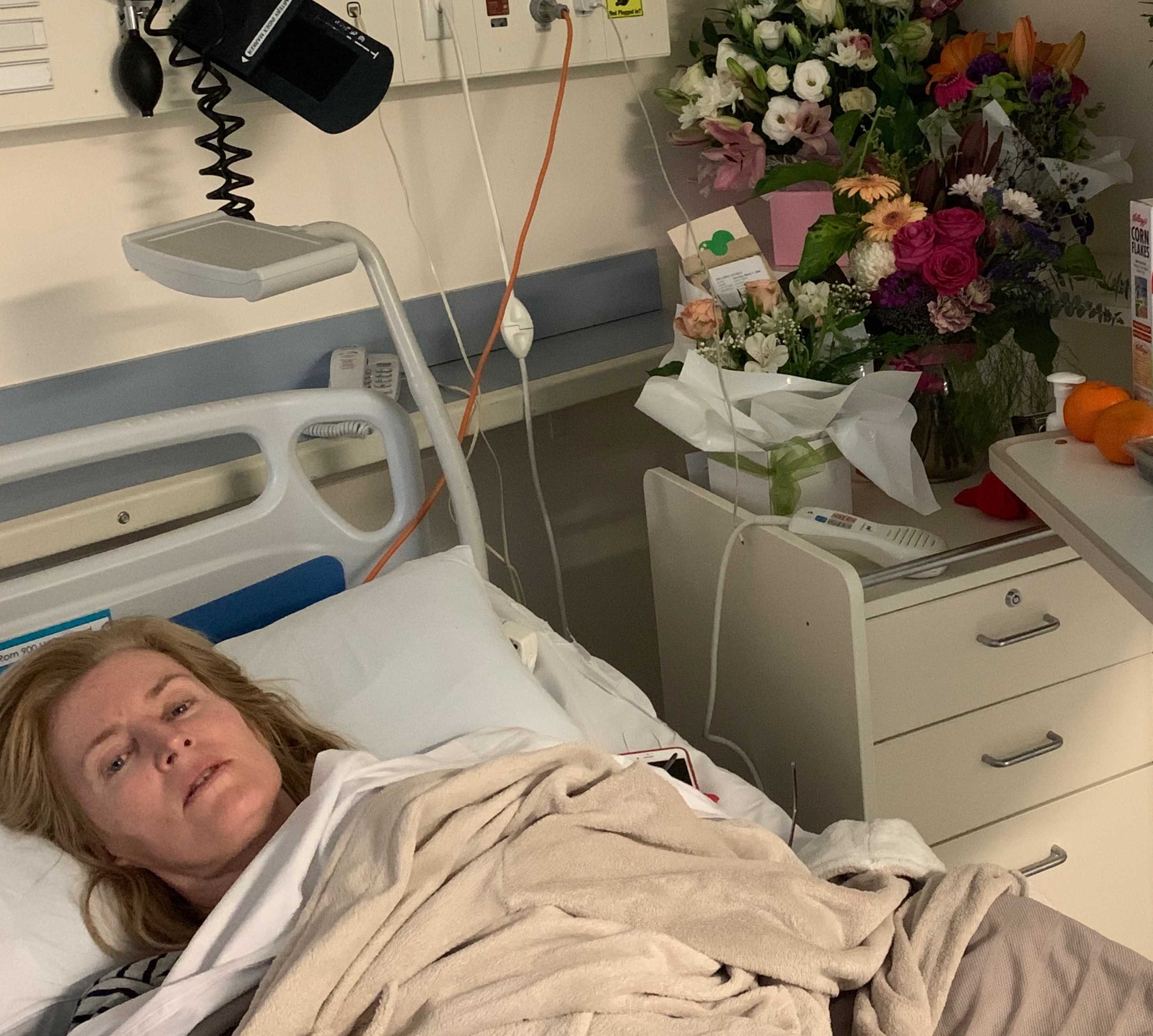 Woman lying in hospital bed looking very sick with flowers on side table.