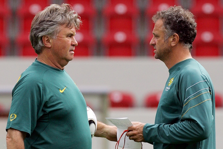 在 Socceroos 练习课期间，两名身着澳大利亚装备的教练站在球场上谈论战术。