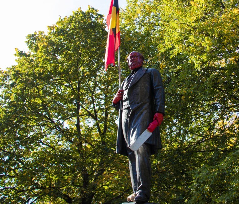 A statue of a colonial man holding and Aboriginal flag, with red face and hands
