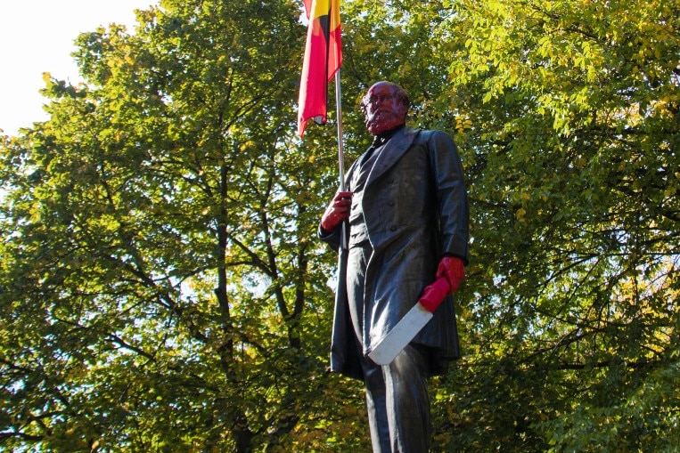 A statue of a colonial man holding and Aboriginal flag, with red face and hands