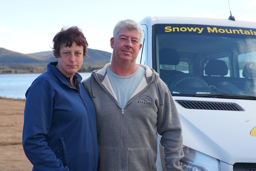 A woman and a man standing next to a shuttle bus by the lake.
