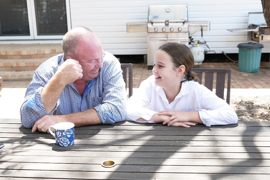 Andrew and Flo Crowe sit at a wooden table on the back patio of the farm house.