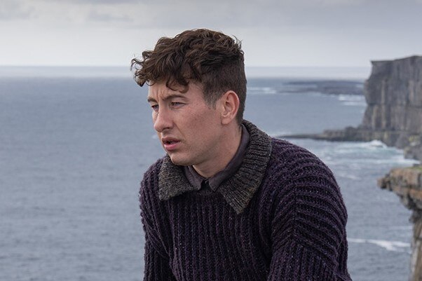 a still of Barry Keoghan in The Banshees of Inisherin. He's sitting on a wall in front of the ocean.
