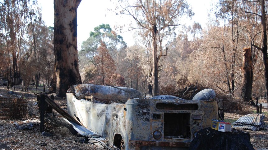 A vehicle lies burnt and destroyed among the debris of a bushfire at a property