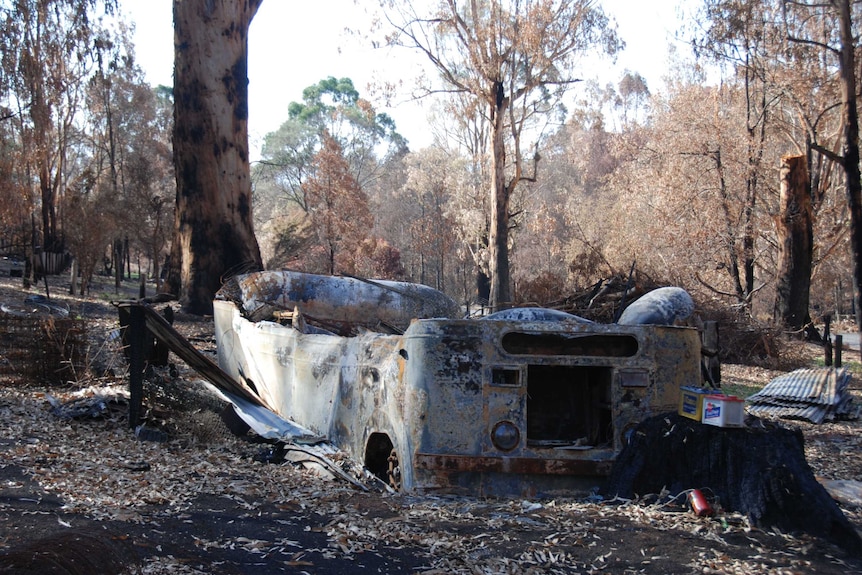 A vehicle lies burnt and destroyed among the debris of a bushfire at a property