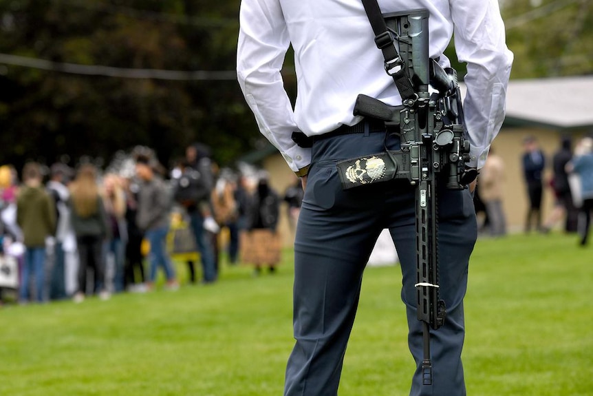 A man carrying a very huge gun in a park with people in the background