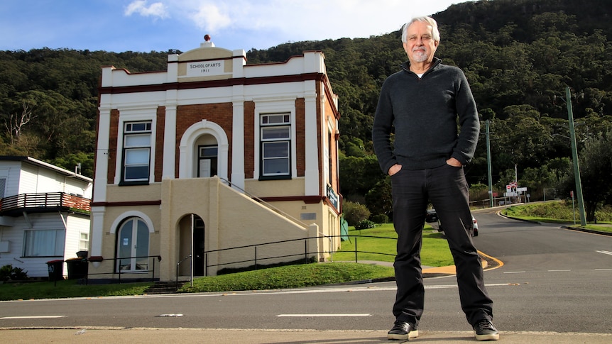 David Roach stands in a black jumper and jeans across the road from the Clifton School of Arts building.