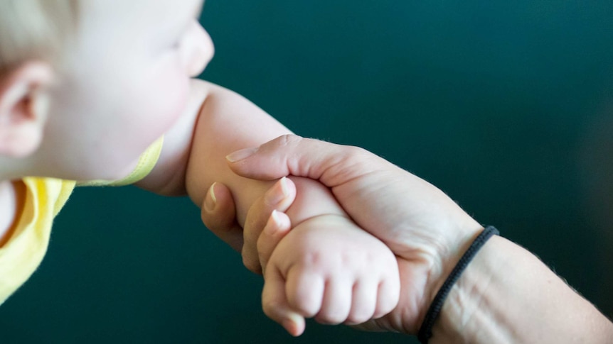 Mother holding the wrist of a baby who is out of focus.
