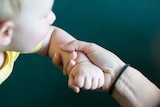 Mother holding the wrist of a baby who is out of focus.