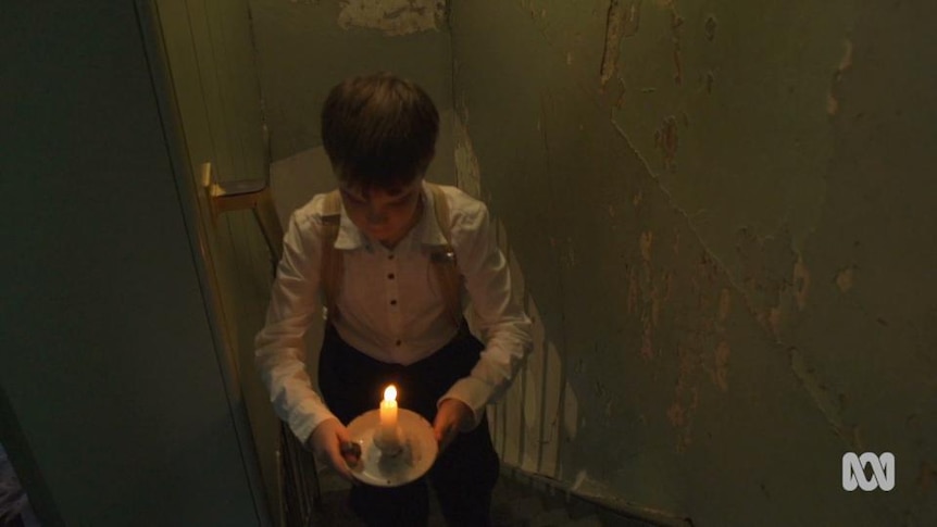 Boy walks up stairs with lit candle