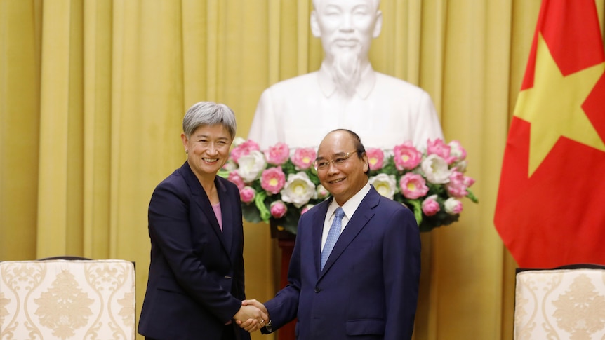 Penny Wong and Nguyen Xuan Phuc shake hands in front of a white bust of Ho Chi Minh with Vietnamese flag of yellow star on red 