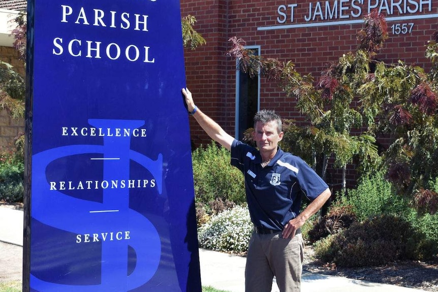 Peter Fahey leaning on the school sign with one hand.