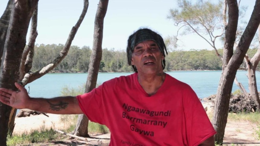 Indigenous man stands beside body of water