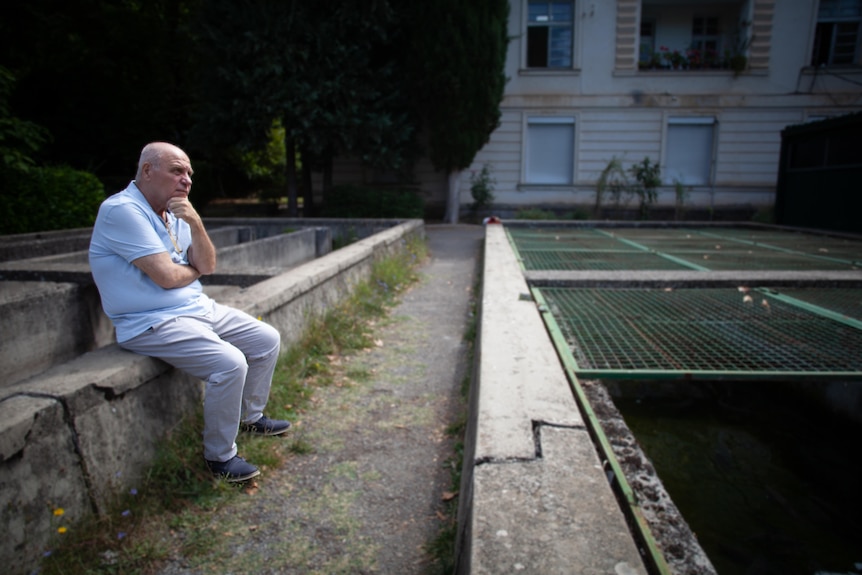 An elderly man sitting on a short fence next to grates