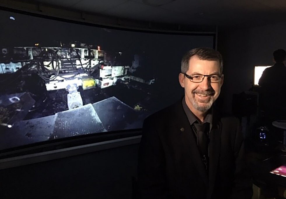 Dr Mark Dunn sits in a darkened room in front of a virtual reality screen showing an underground coal mine.