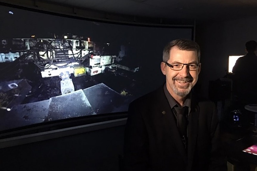 Dr Mark Dunn sits in a darkened room in front of a virtual reality screen showing an underground coal mine.