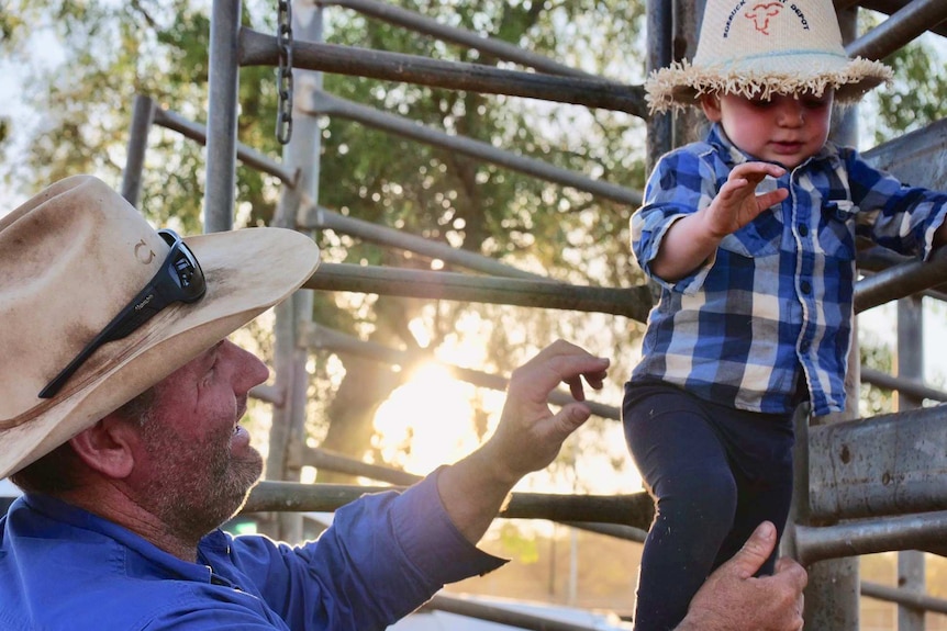 Man holds his son next to cattle yards