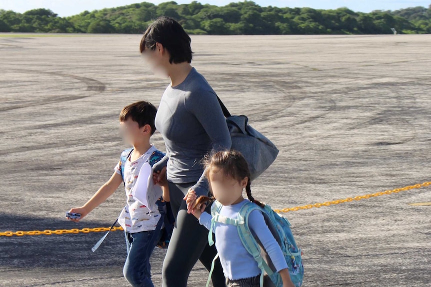 A woman and two children walk across an airport runway.