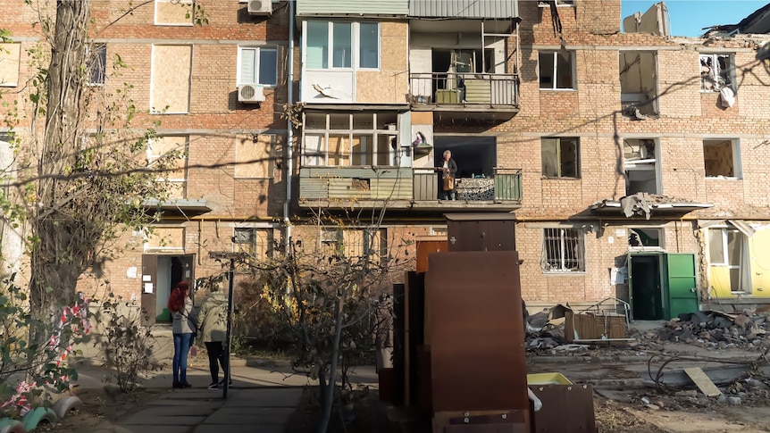 Several people stand outside a damaged apartment building in Ukraine.