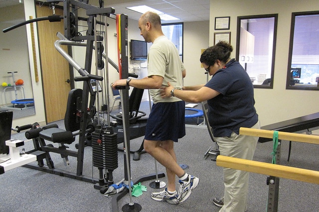 A man goes through a physical therapy session and is assisted through a leg exercise by his physio
