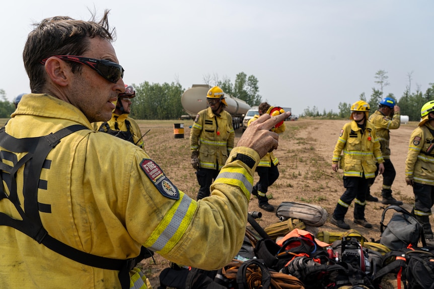 Firefighters in yellow uniforms stand around equipment on the ground in a field.