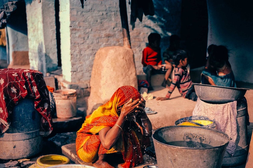 A women throws water over her head in an Indian slum.